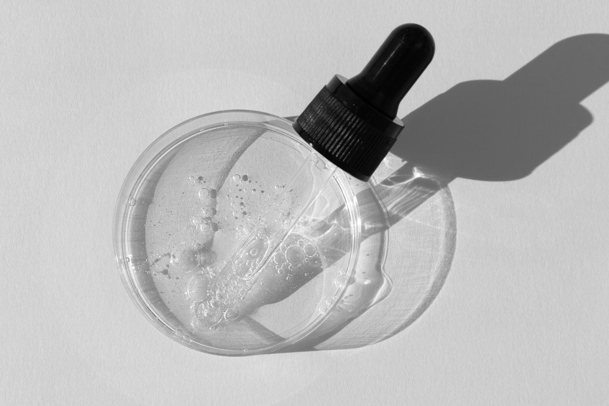 Serum for the face, oil, fluid or gel with a pipette in Petri dish on a gray background. Concept of cosmetics laboratory researches, wellness and beauty